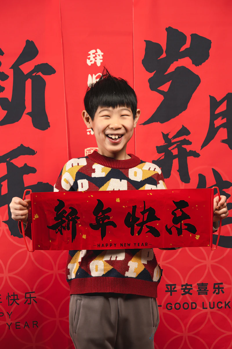 A smiling boy holding a red banner that says 新年快乐, Happy New Year