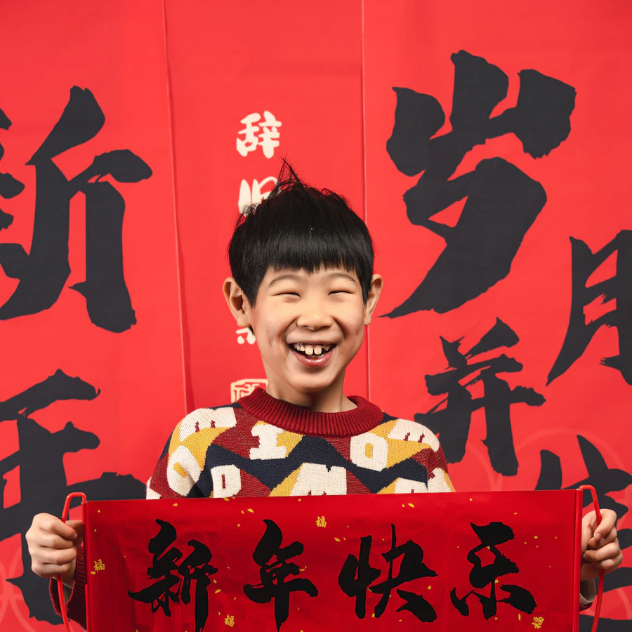 A smiling boy holding a red Happy New Year banner