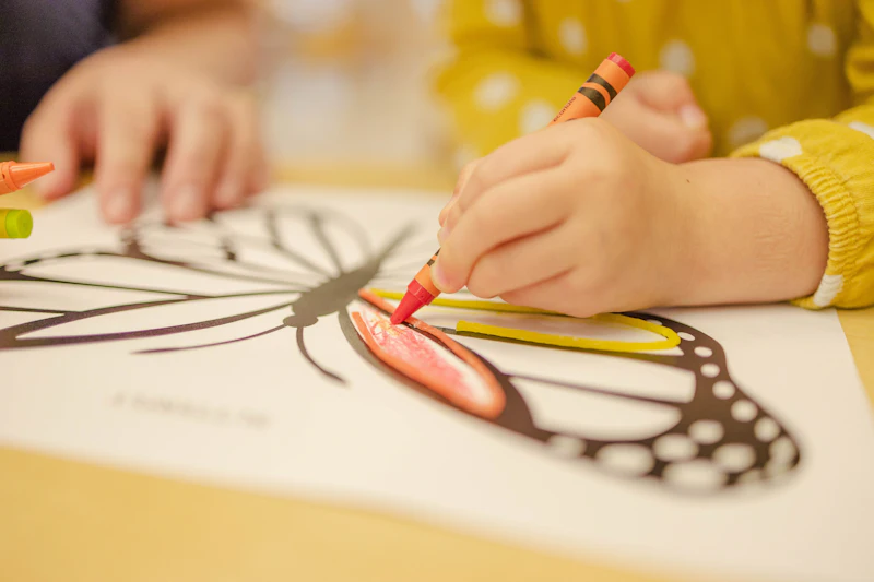 A child colouring a butterfly with a red crayon