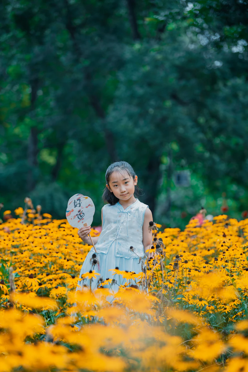 A young girl holding a fan in a field of yellow flowers