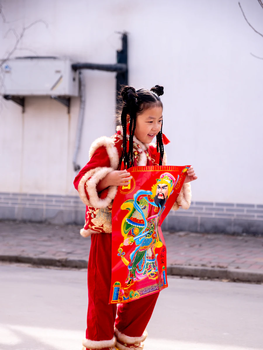 A young girl in a red festival jacket holding a New Year picture